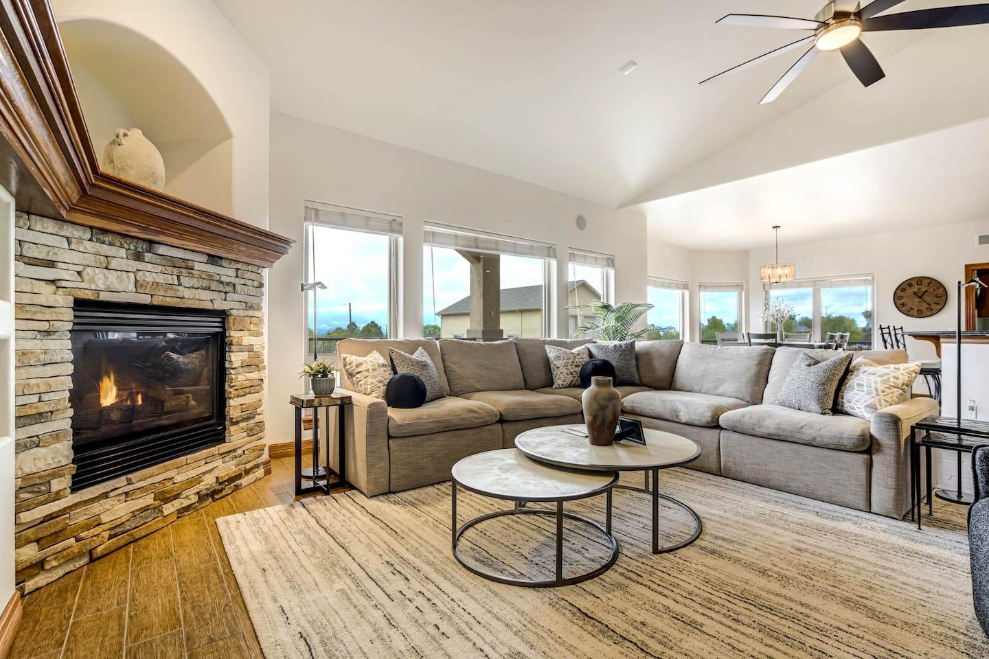 Living room with a stone gas fireplace, sectional sofa and a wall of windows facing the mountains