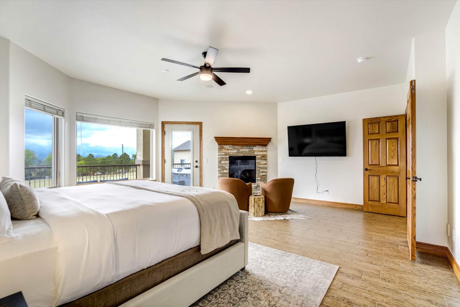 Primary suite with a king bed in white bedding, a stone gas fireplace and windows facing the mountains